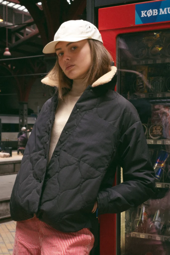 Model wearing a black and nylon jacket, standing in a train station.